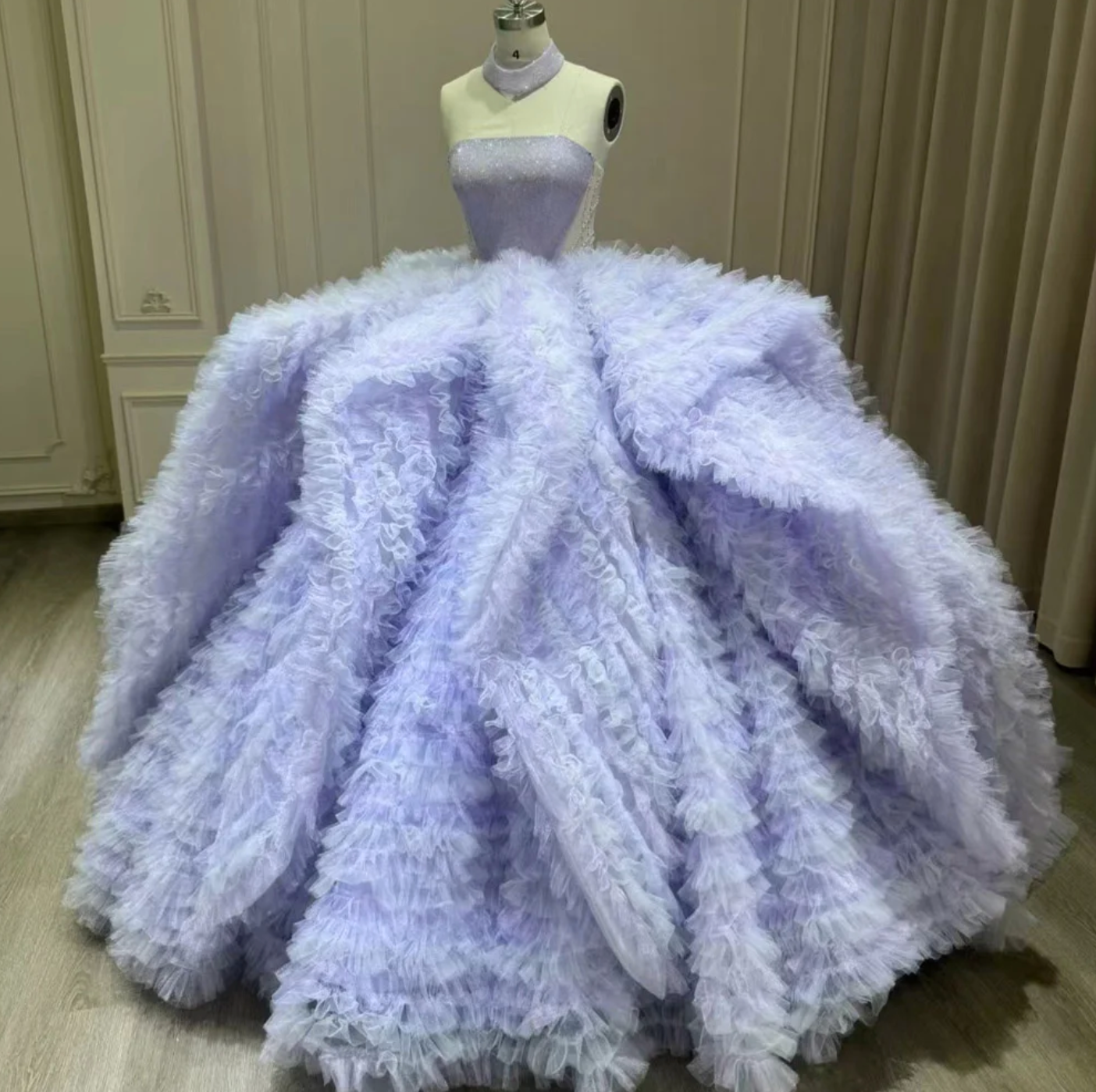 Lavender 3D floral ball gown dress on a mannequin, featuring ruffled layers and a sparkling bodice, ideal for Quinceanera.