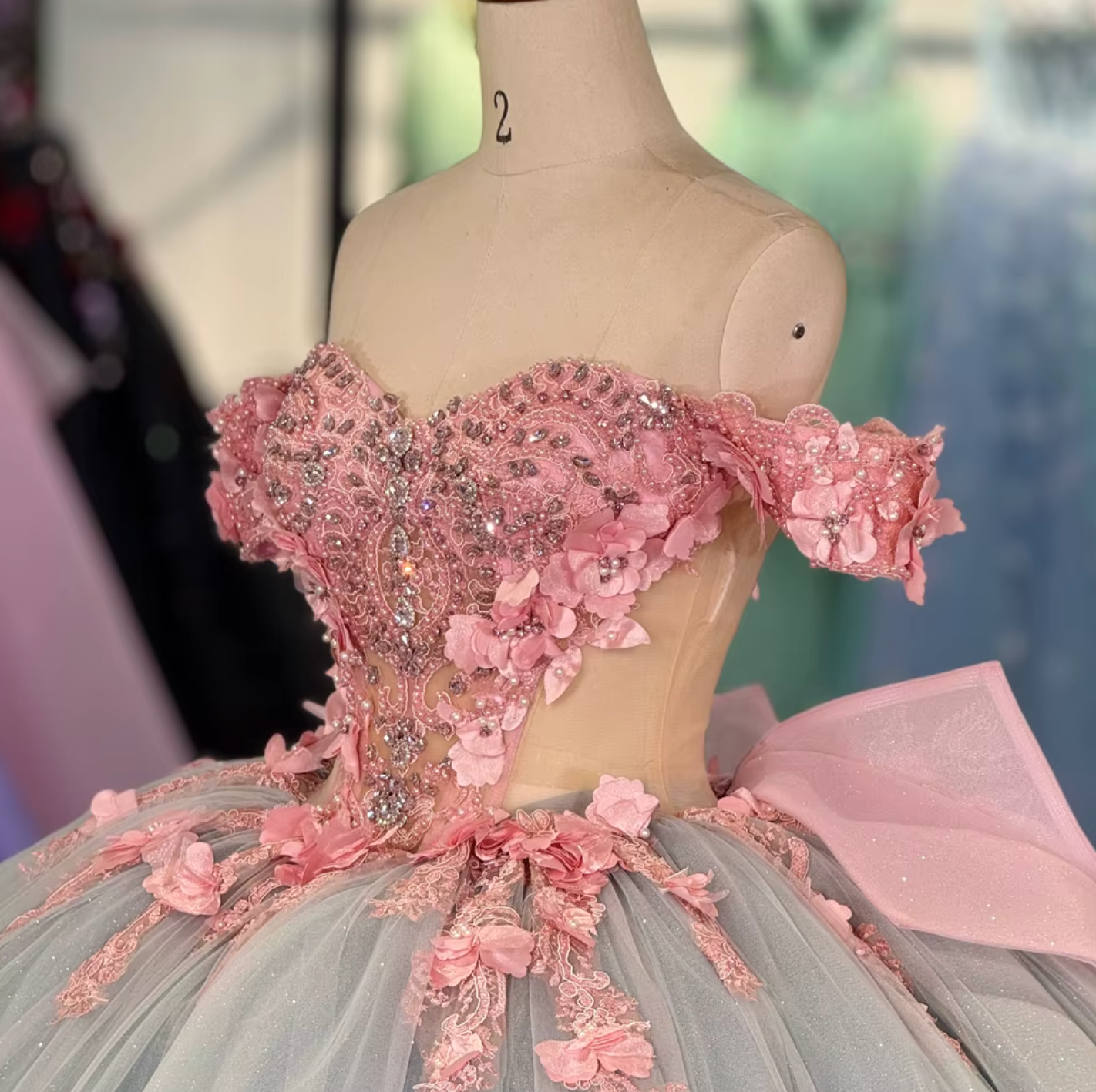A stunning blue and pink Quinceanera dress with a sheer lace bodice, 3D floral decorations, a sweetheart neckline, and a full ballroom skirt with an oversized back bow.