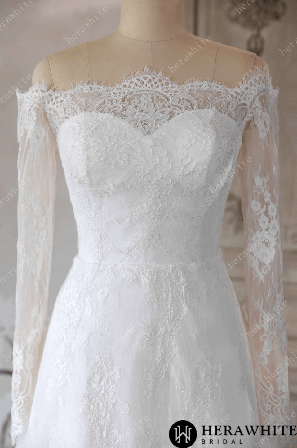 White lace wedding dress on a mannequin against a decorative wall.