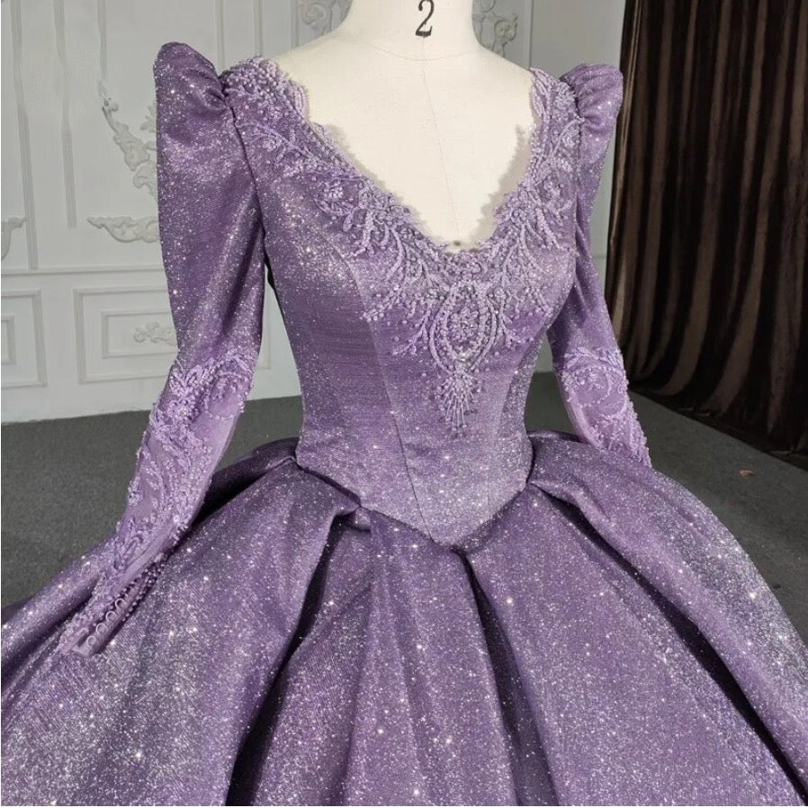 Close-up of a purple long sleeve A-line ball gown featuring sparkling fabric and intricate beading on the bodice.