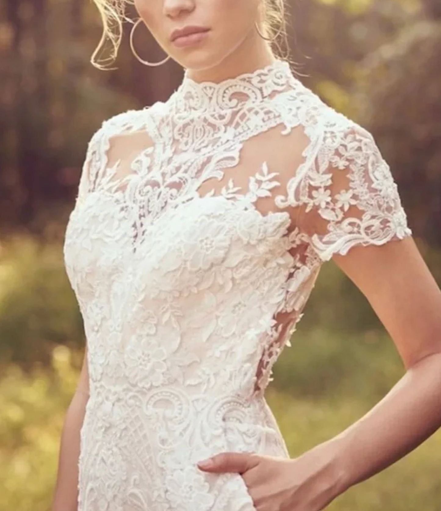 Close-up of a bride in a white lace wedding dress with floral patterns and short sleeves, set in a natural background.