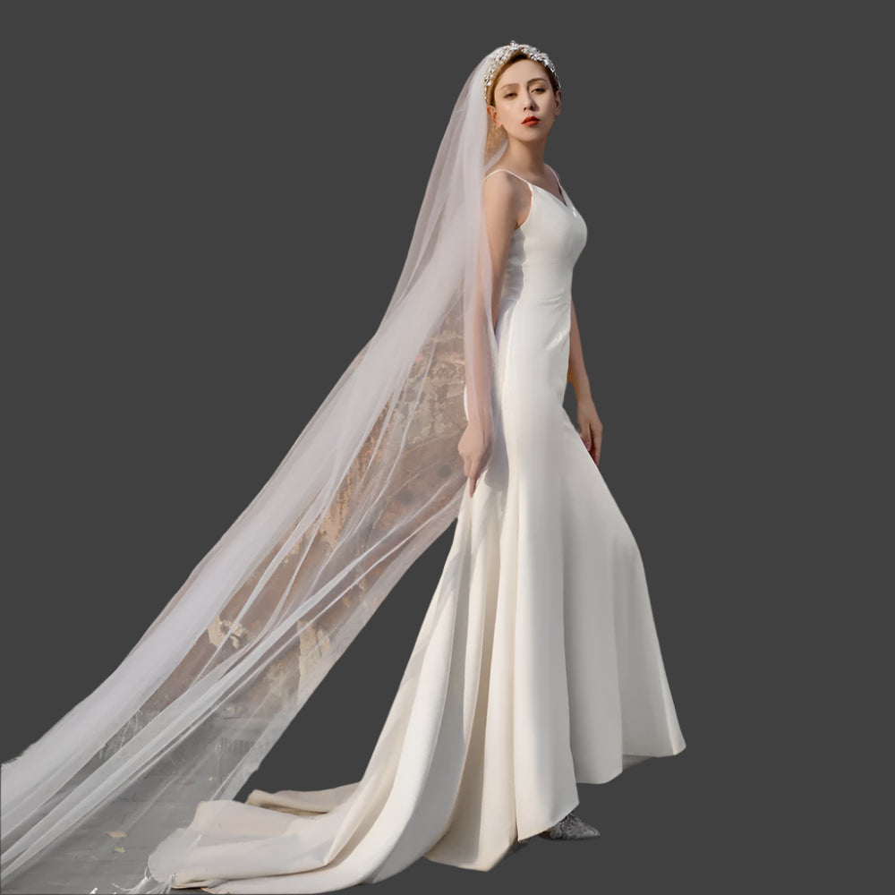 Woman in a white wedding dress with a long veil standing against a textured, dark background.