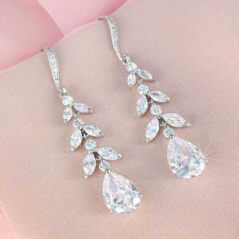 Silver teardrop and leaf-shaped crystal earrings on a person's hand.