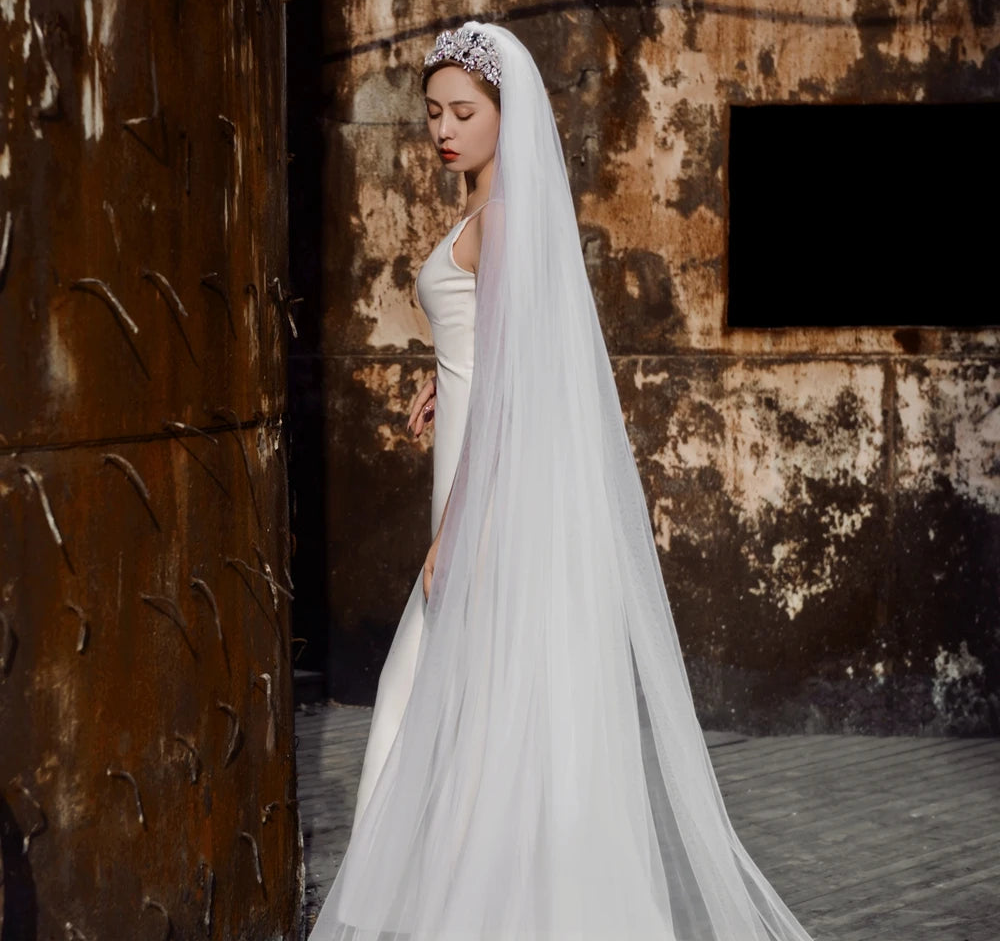 
                      
                        Woman in a white wedding dress with a long veil standing against a textured wall.
                      
                    