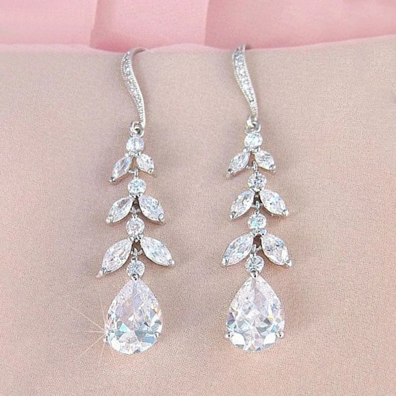 Pair of silver teardrop earrings with clear gemstones on a pink background