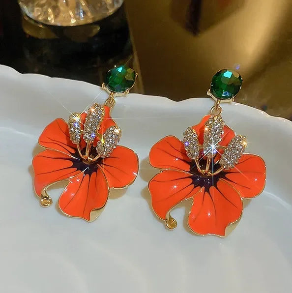Floral earrings with orange flowers and green gemstones on a white plate.