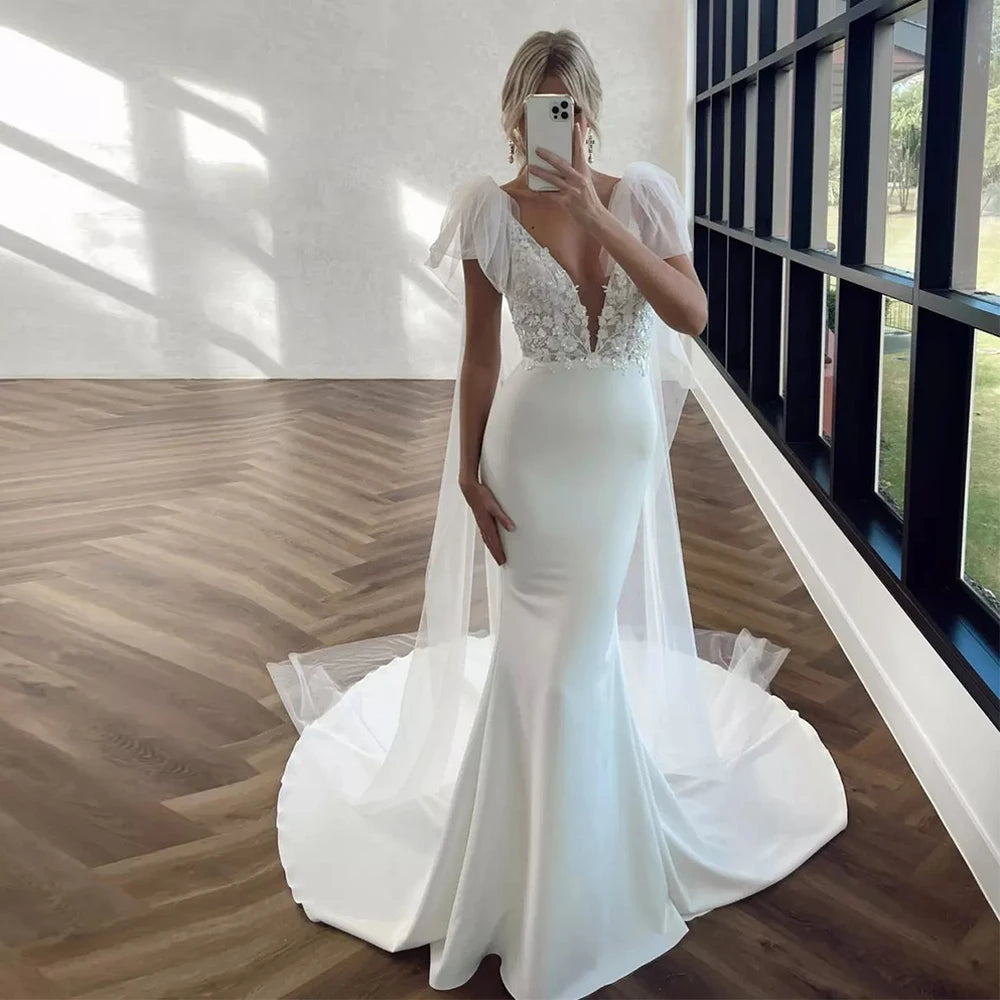 
                      
                        Woman in a white wedding dress standing in a room with wooden flooring and large windows.
                      
                    