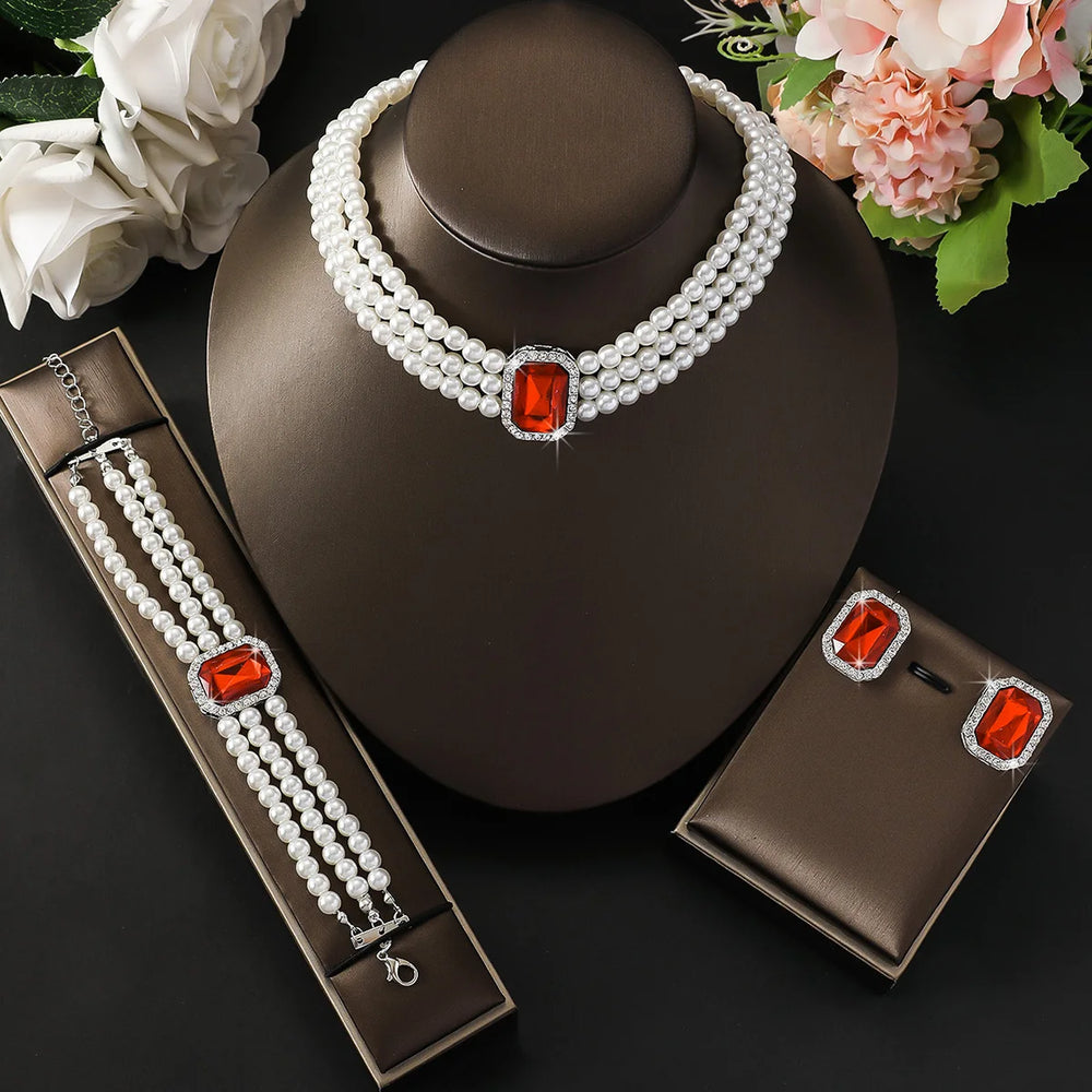 
                      
                        Pearl jewelry set with red gemstones on a dark surface with flowers.
                      
                    