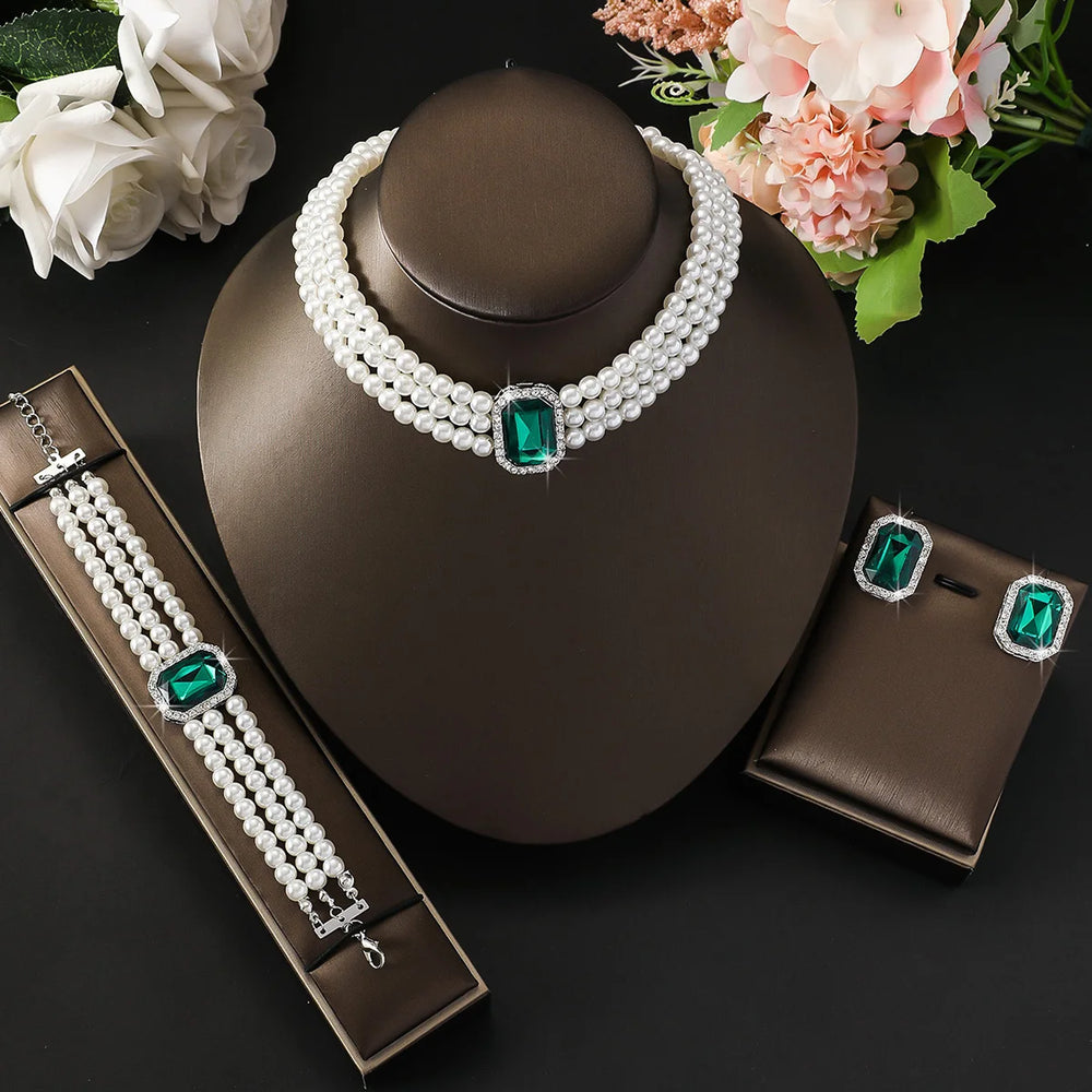 Pearl jewelry set with green gemstones on a dark surface with flowers.
