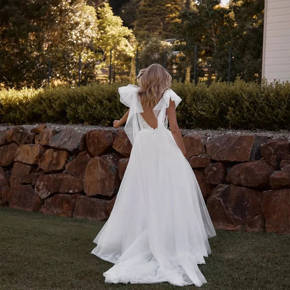 
                      
                        Woman in a white wedding dress standing in front of a stone wall with trees in the background
                      
                    
