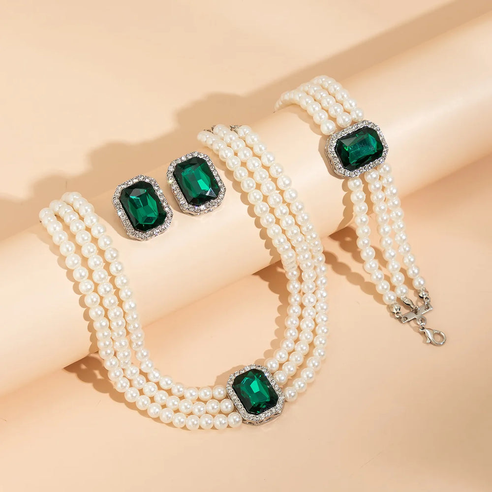 
                      
                        Pearl necklace and bracelet set with green gemstones on a beige background
                      
                    