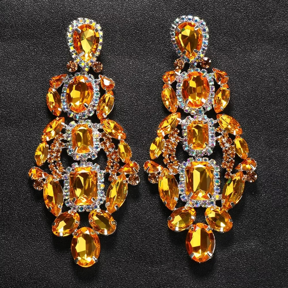
                      
                        Pair of ornate earrings with orange gemstones on a dark background
                      
                    