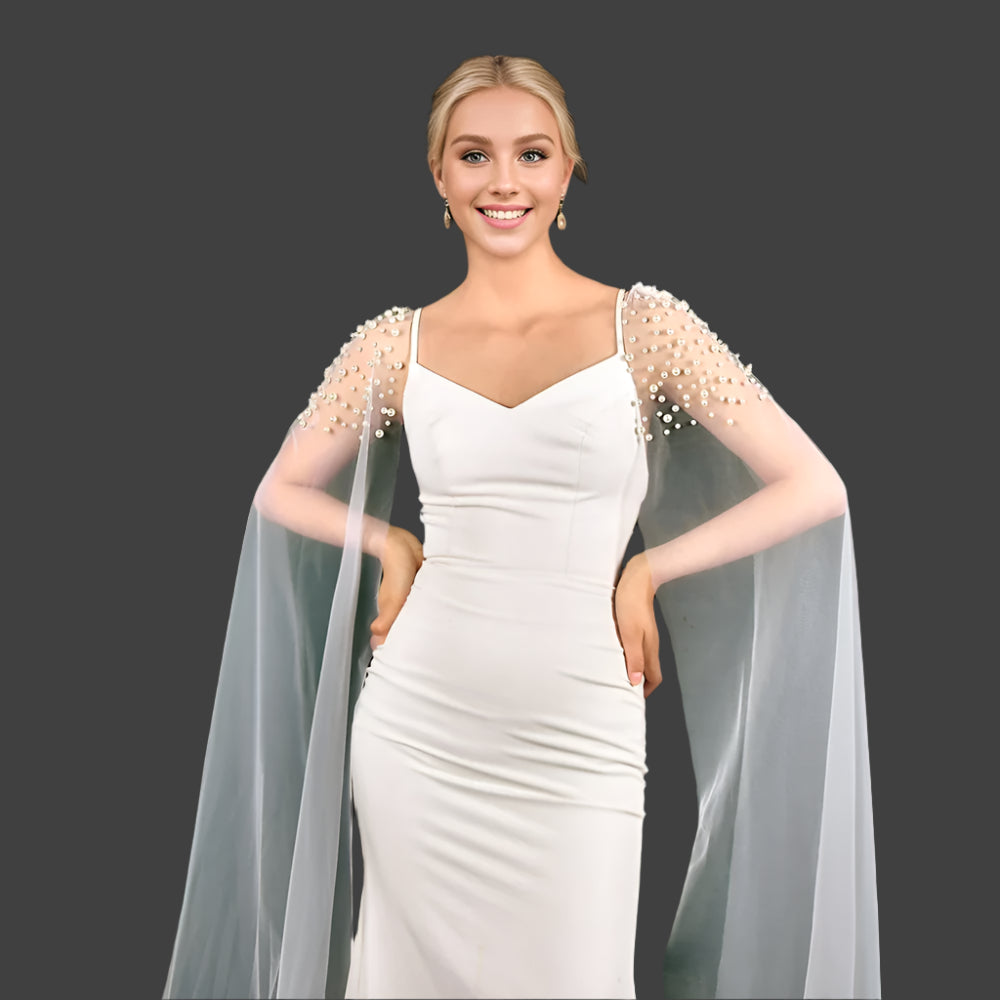
                      
                        Woman in a white dress with sheer sleeves and cape, posing indoors.
                      
                    