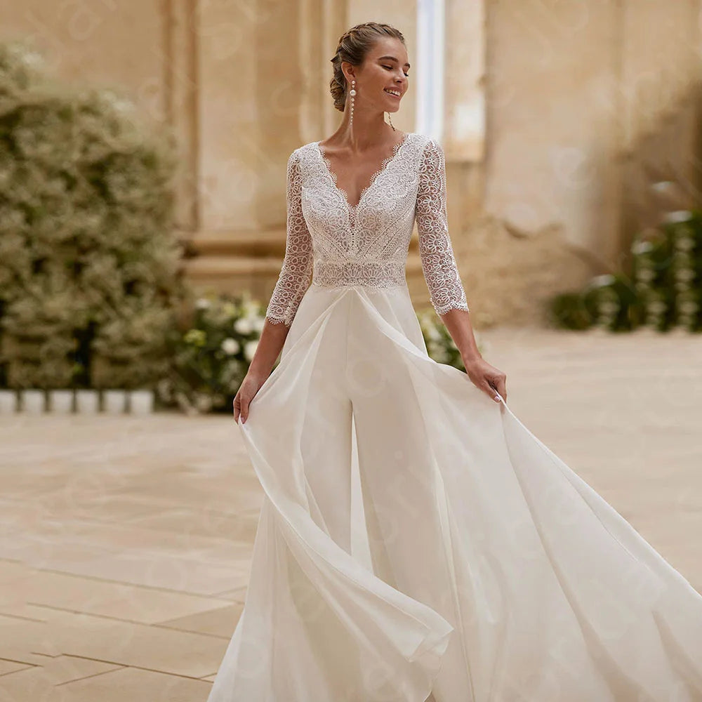 Woman in a white wedding  jumpsuit dress with lace detailing standing outdoors.