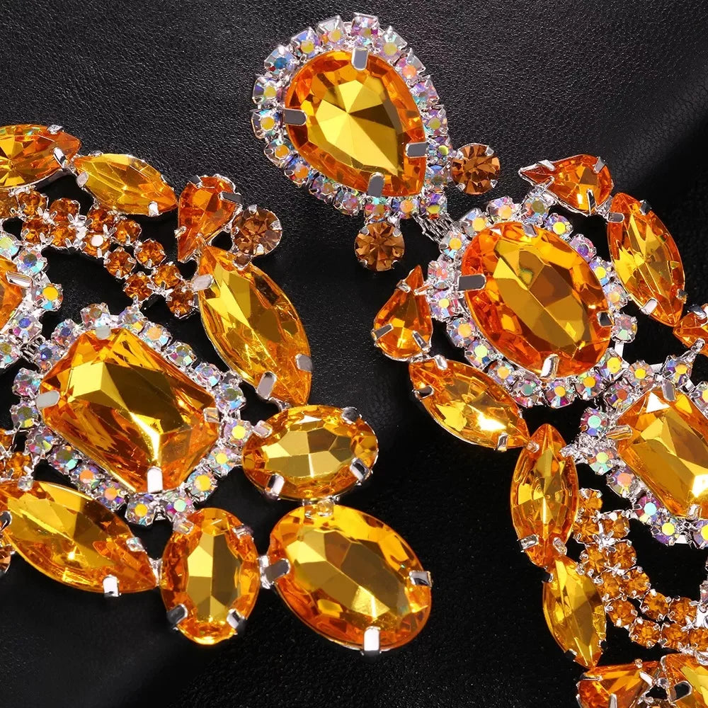 
                      
                        Ornate earrings with orange and clear gemstones on a black background
                      
                    