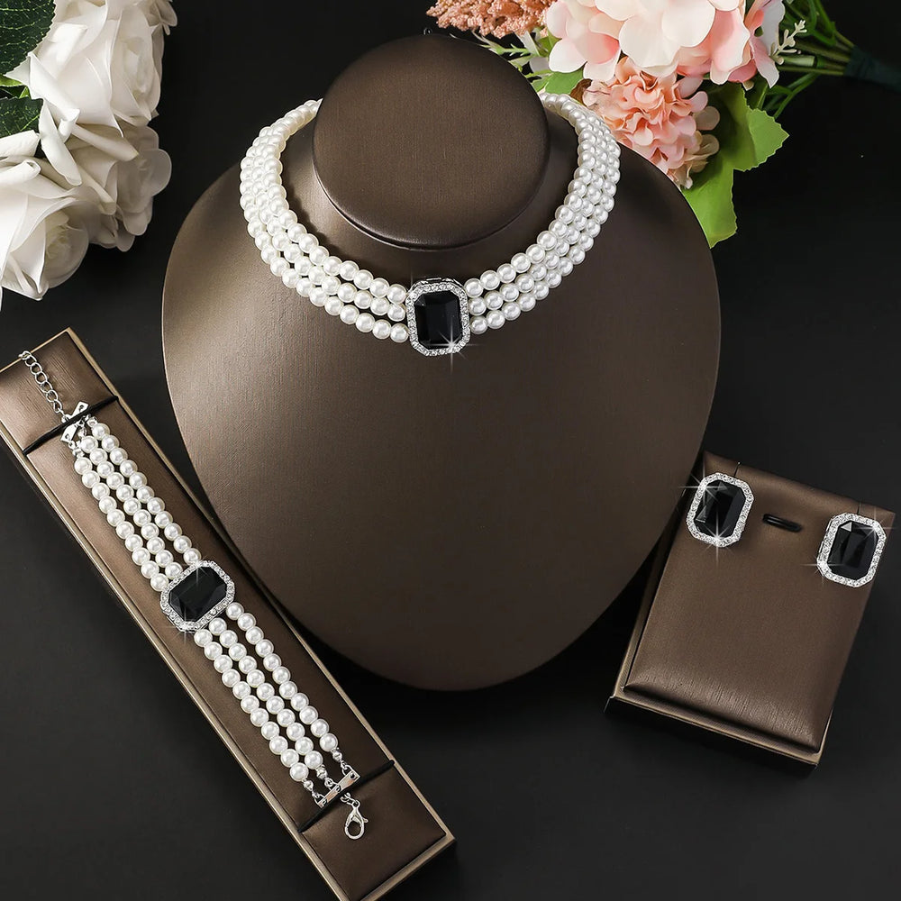 
                      
                        Pearl necklace with black accents on a brown mannequin bust, accompanied by a bracelet and earrings, with flowers in the background.
                      
                    