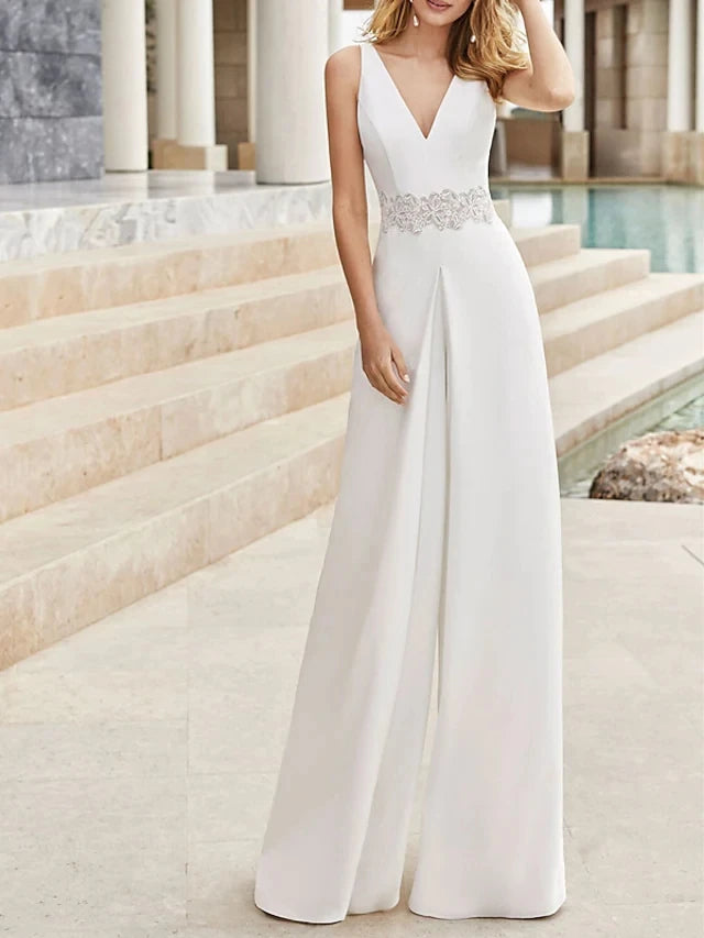 Woman wearing a white gown jumpsuit with a beaded waistband in an outdoor setting.