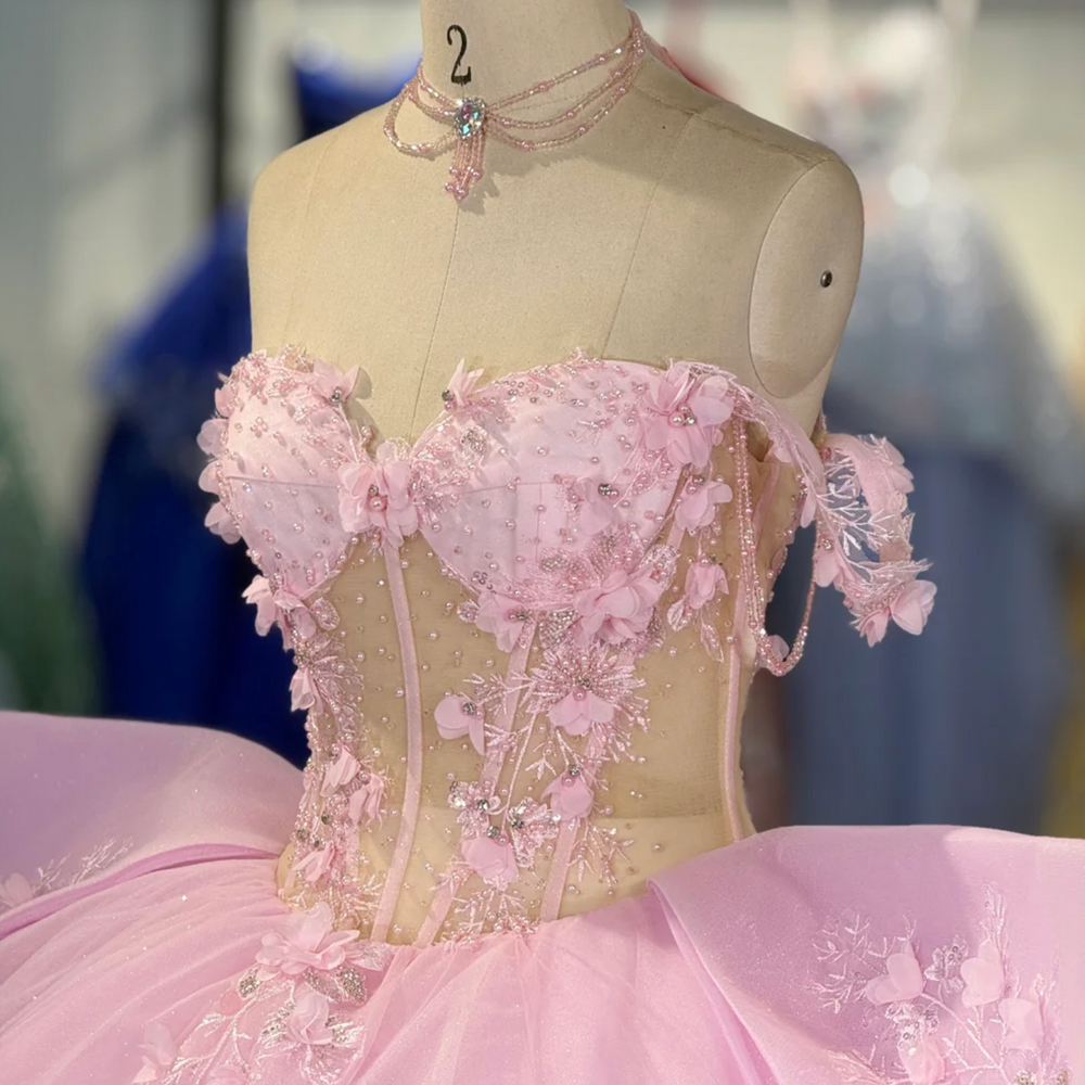 
                      
                        Pink evening gown with floral details on a mannequin in a room with other colorful dresses.
                      
                    