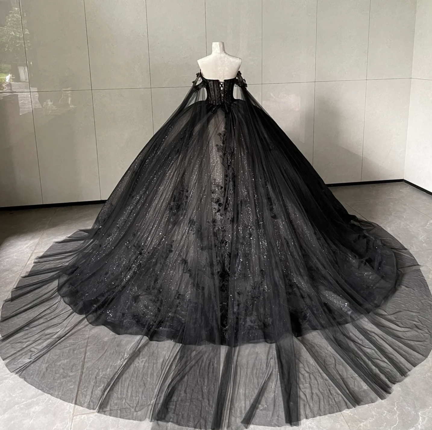 Black evening gown on a mannequin against a gray tiled wall
