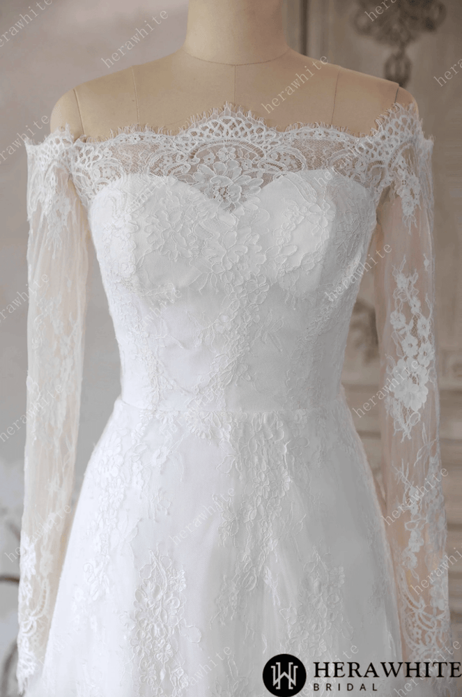 
                      
                        White lace wedding dress on a mannequin against a decorative wall.
                      
                    