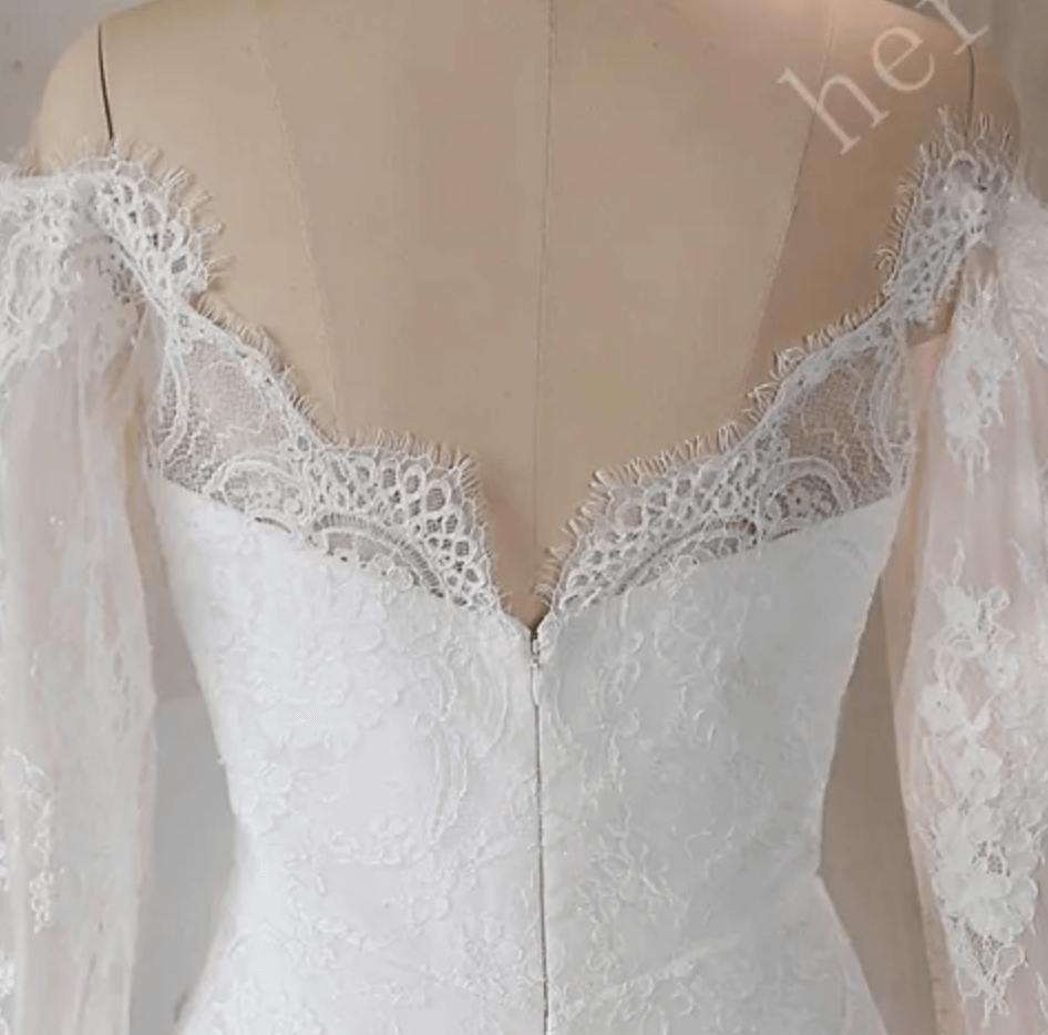 
                      
                        Vestido de novia moderno y glamoroso con hombros descubiertos, abertura hasta el muslo y delicadas mangas de encaje.
                      
                    