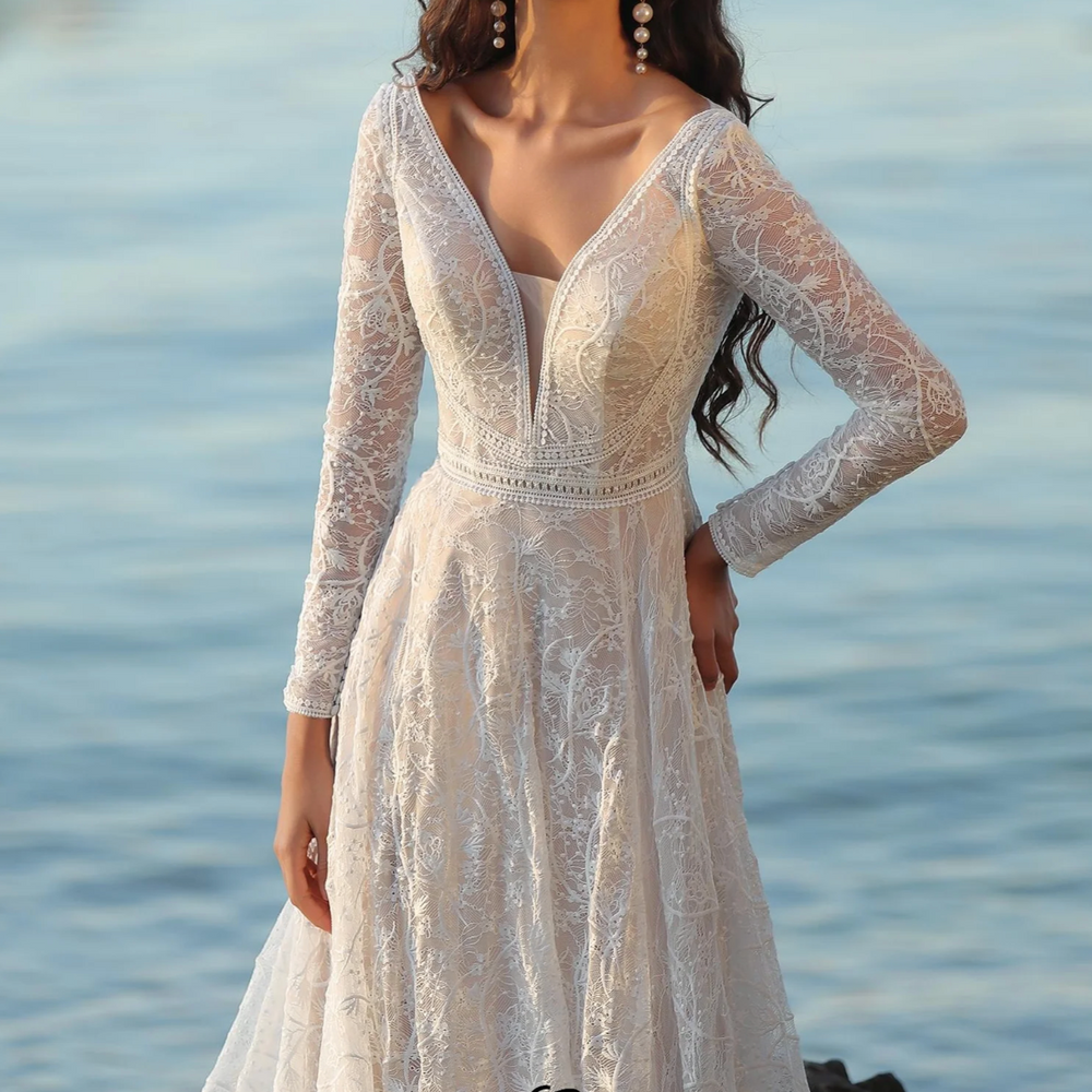 
                      
                        Elegant boho A-line wedding dress with V-neckline and long sleeves, crafted in delicate lace against a serene backdrop.
                      
                    