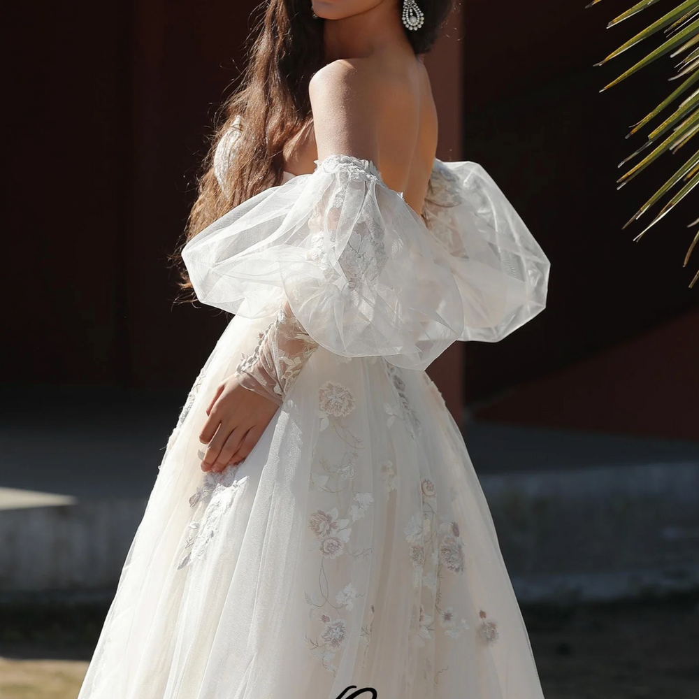 
                      
                        Whimsically romantic wedding gown with puffed sleeves and delicate embroidery, model showcasing elegant A-line design.
                      
                    