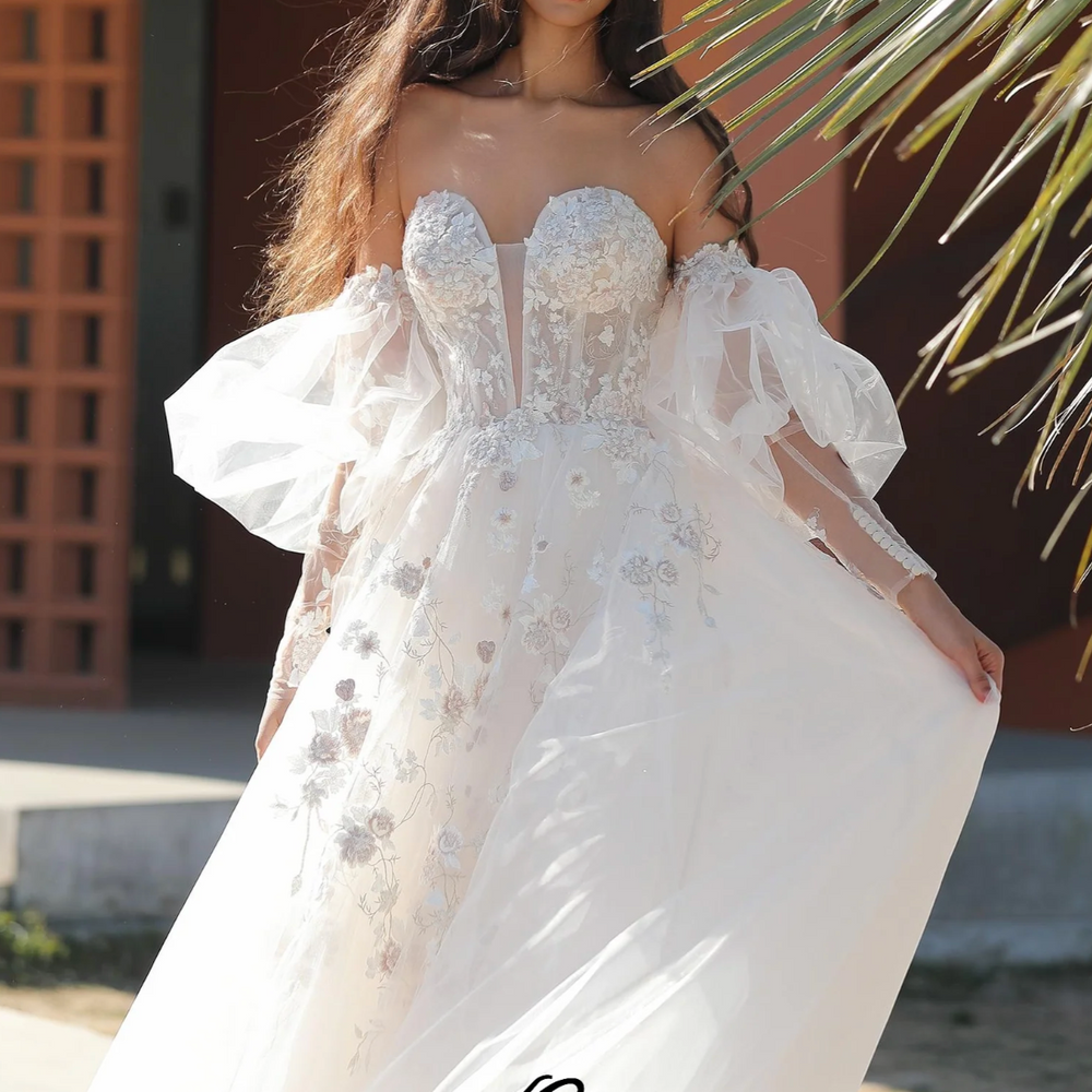 
                      
                        Wedding gown with puffed sleeves, sweetheart neckline, and delicate embroidery, embodying whimsical romance.
                      
                    