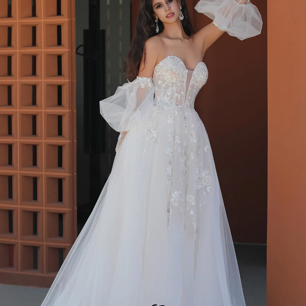 
                      
                        Romantic wedding gown with puffed sleeves, lace appliqués, and a sweetheart neckline, perfect for a whimsical bridal look.
                      
                    