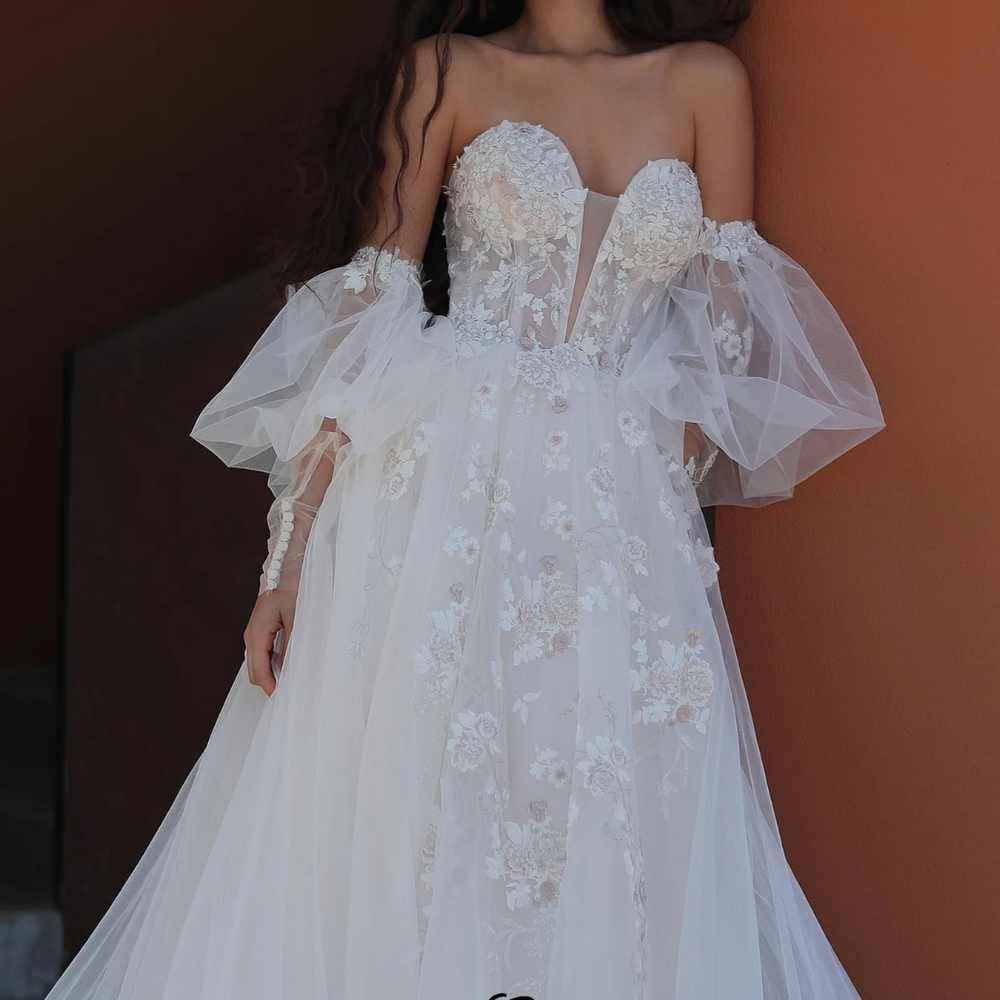 
                      
                        Bridal gown with puffed sleeves, sweetheart neckline, and floral embroidery, exuding whimsical romance.
                      
                    