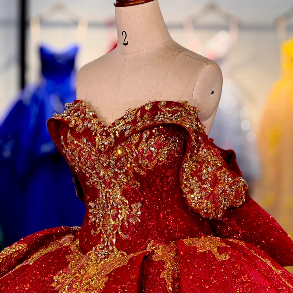 
                      
                        Red evening gown with gold embellishments on a mannequin against a blurred background
                      
                    