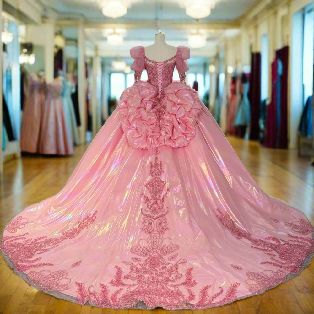 Pink evening gown with intricate detailing on a mannequin in a room with other dresses.