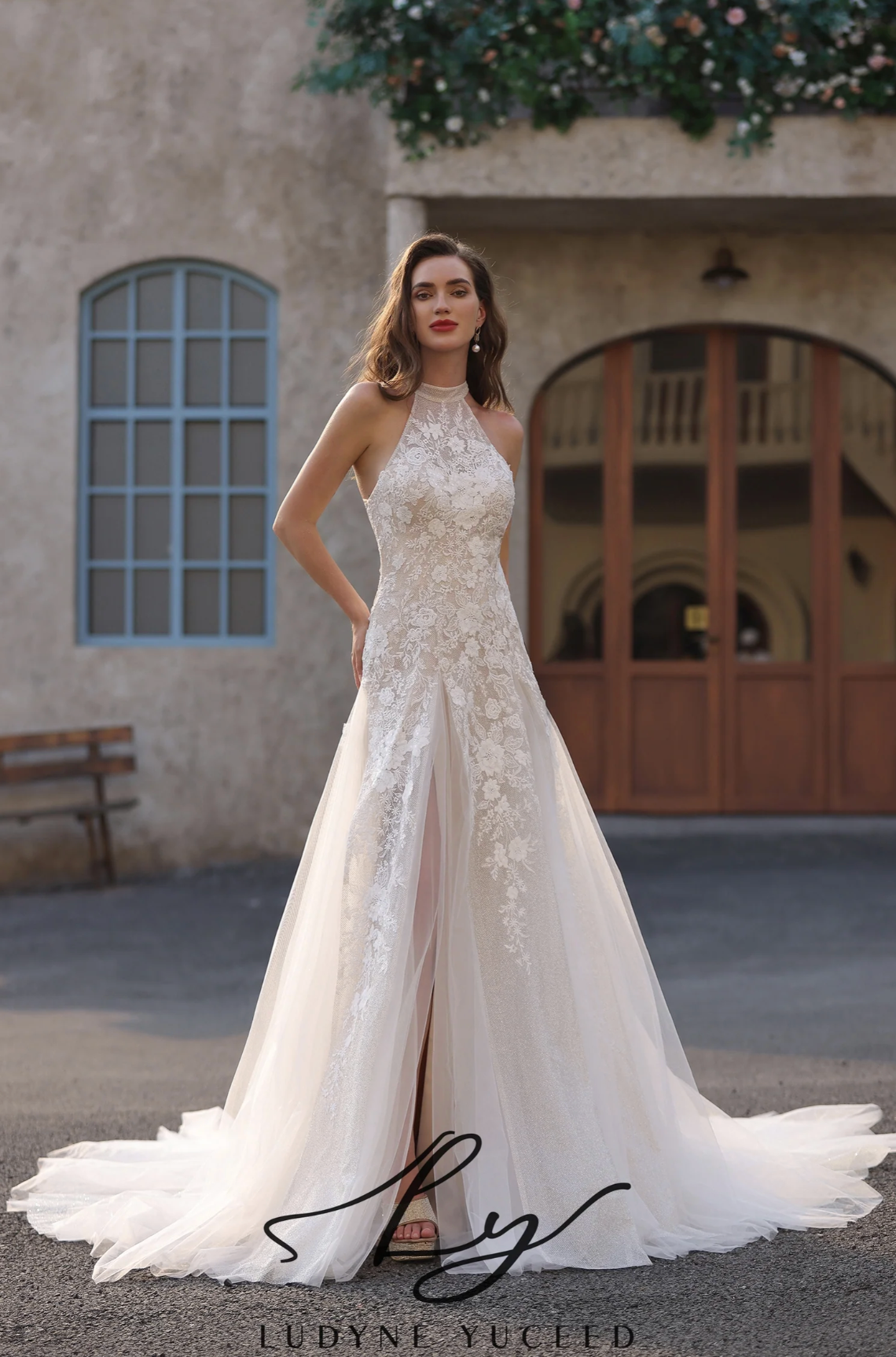 Woman in a white lace wedding dress standing in front of a building with decorative elements.