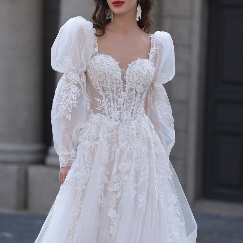 Woman wearing a white lace wedding dress with puffed sleeves in front of a stone building.