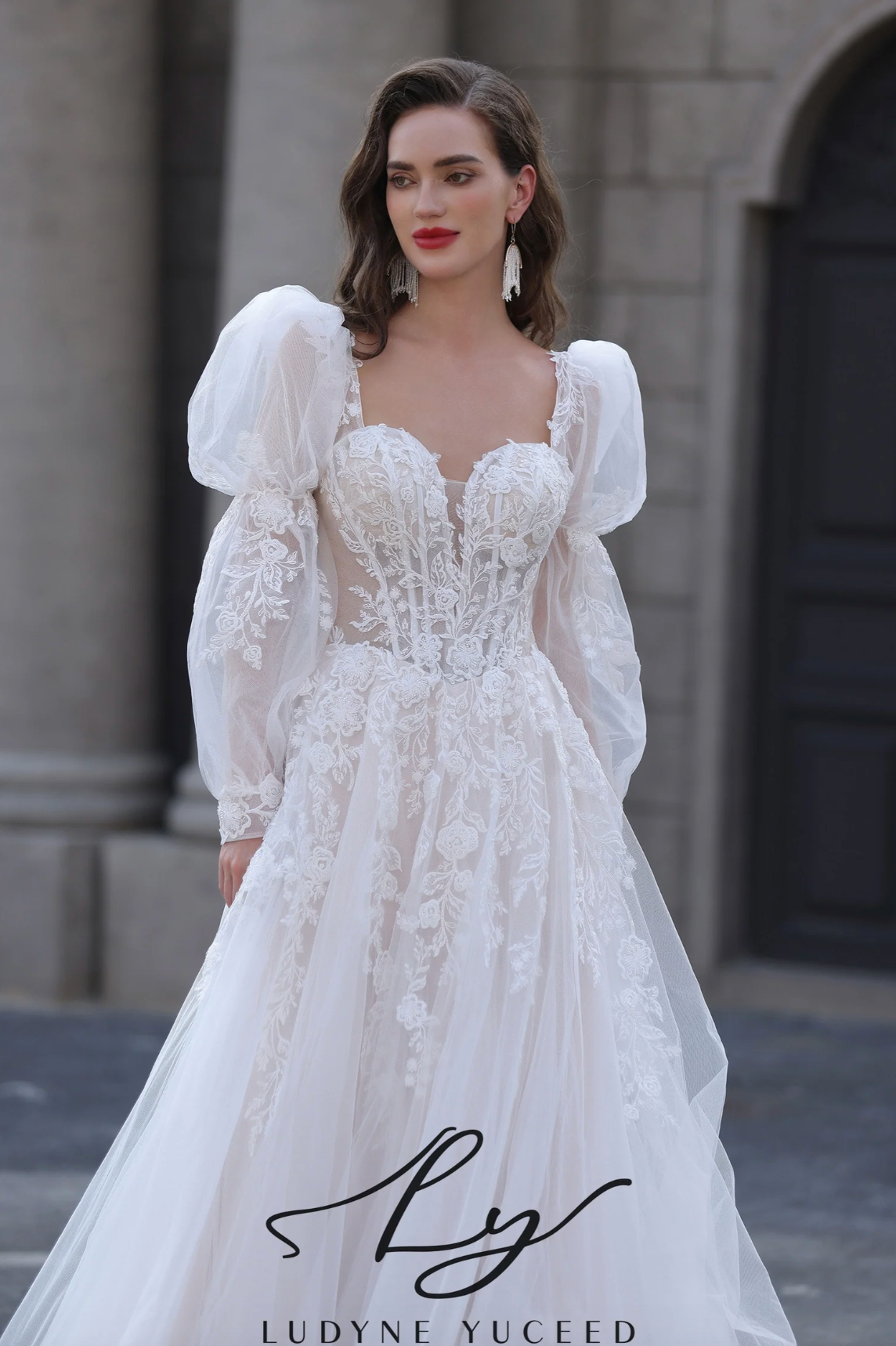 Woman wearing a white lace wedding dress with puffed sleeves in front of a stone building.