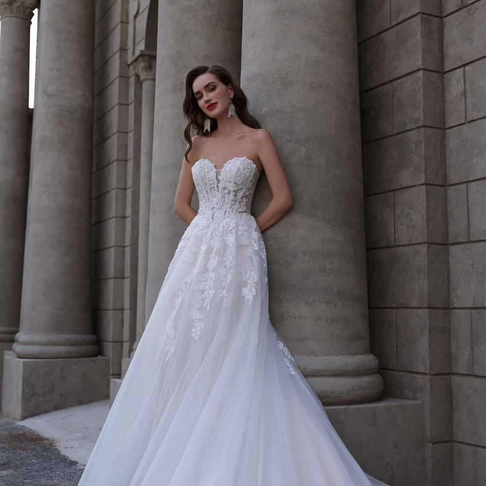 
                      
                        Woman in a white wedding dress standing against a stone building
                      
                    