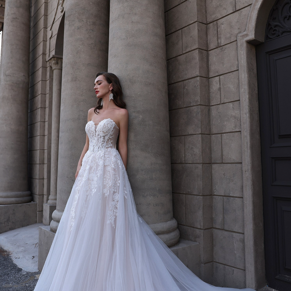 
                      
                        Woman in a white wedding dress standing against a stone building
                      
                    