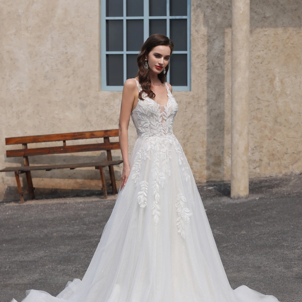 Woman in a white wedding dress standing outdoors with a bench and building in the background.