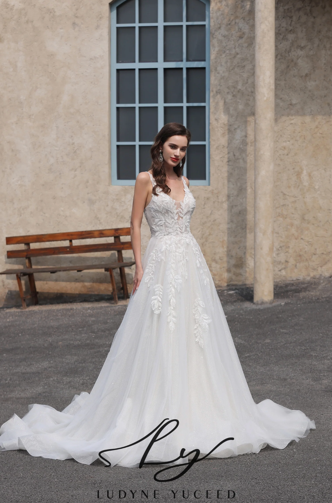 Woman in a white wedding dress standing outdoors with a bench and building in the background.