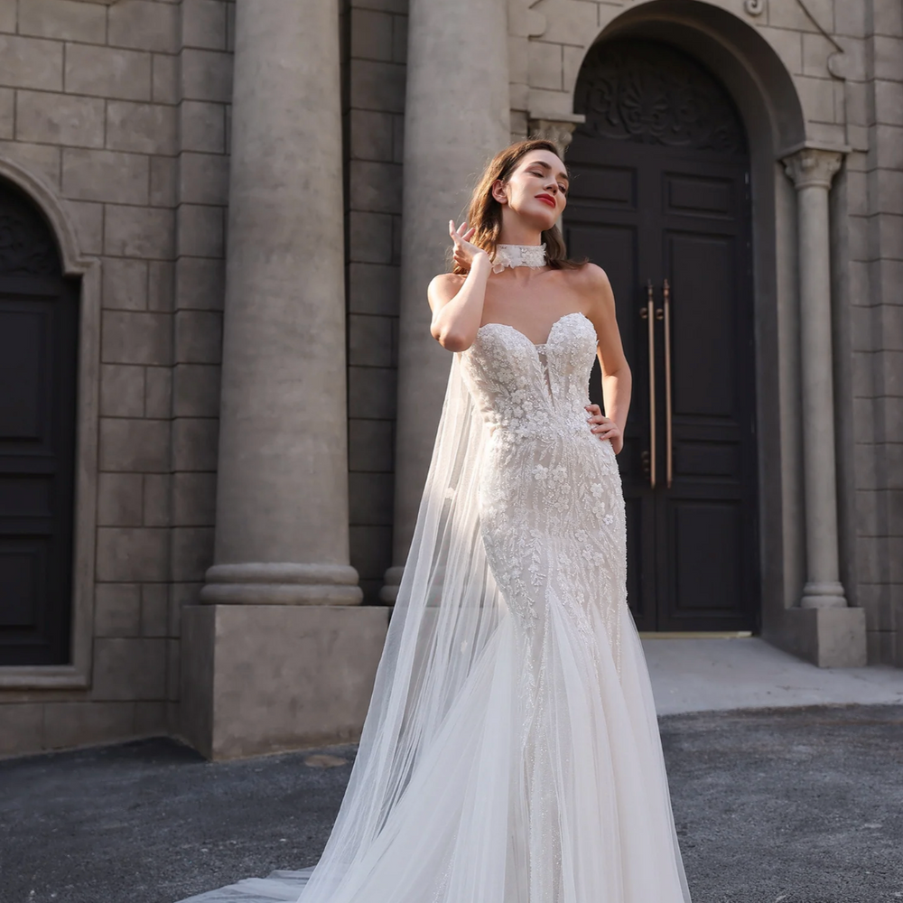 Woman in a white wedding dress standing in front of a stone building with 'Ludyne Yuceld' branding.
