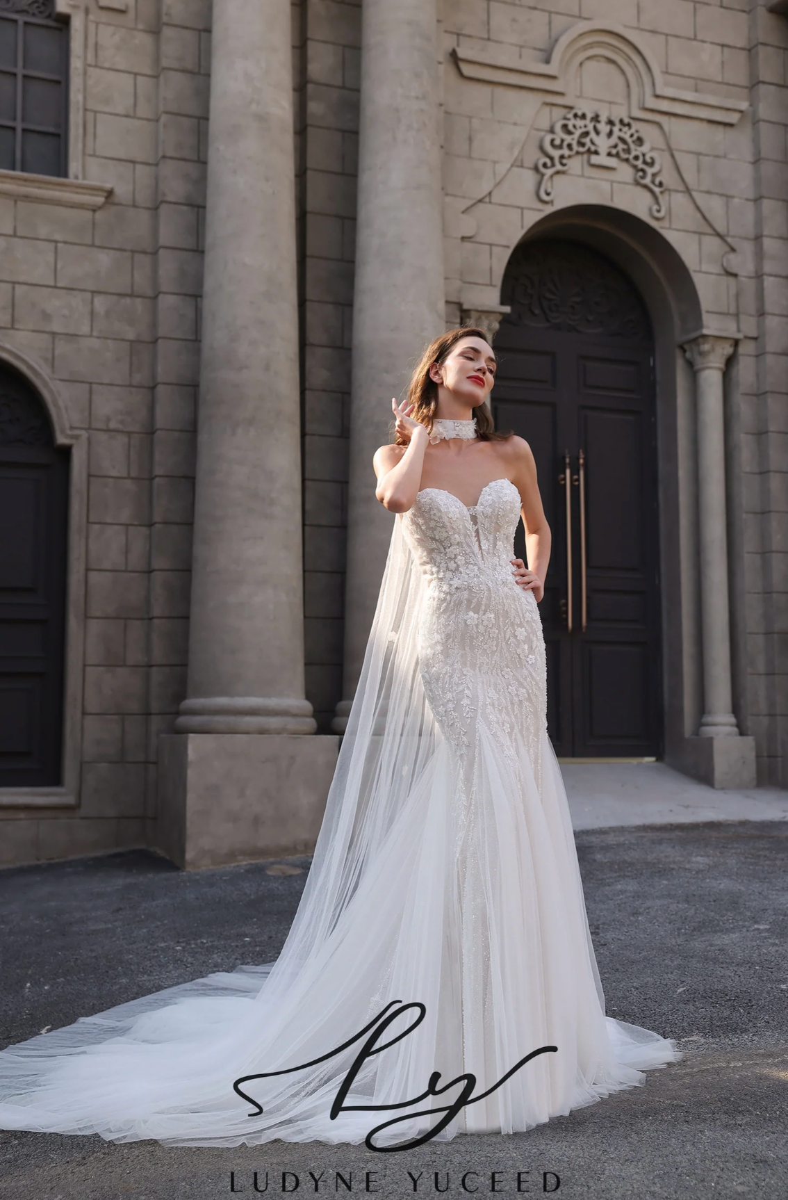 Woman in a white wedding dress standing in front of a stone building with 'Ludyne Yuceld' branding.