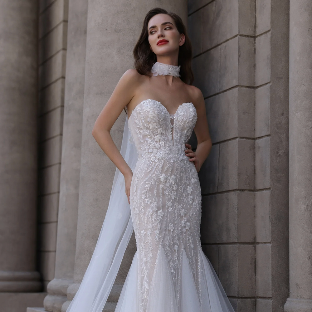 
                      
                        Woman in a white strapless gown standing against a stone wall.
                      
                    