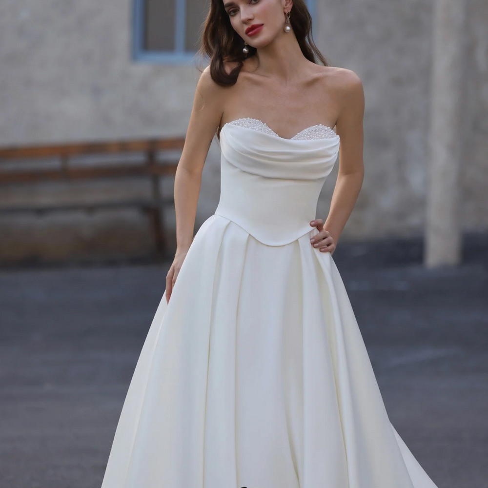 Woman wearing a white strapless dress with 'Ludyne Yuceed' branding in an outdoor setting.