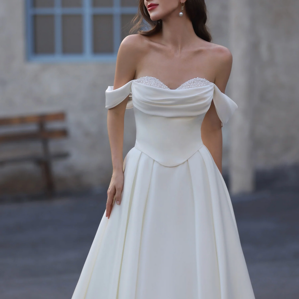 
                      
                        Woman wearing a white off-shoulder gown with 'Ludyne Yuceed' branding in an outdoor setting.
                      
                    