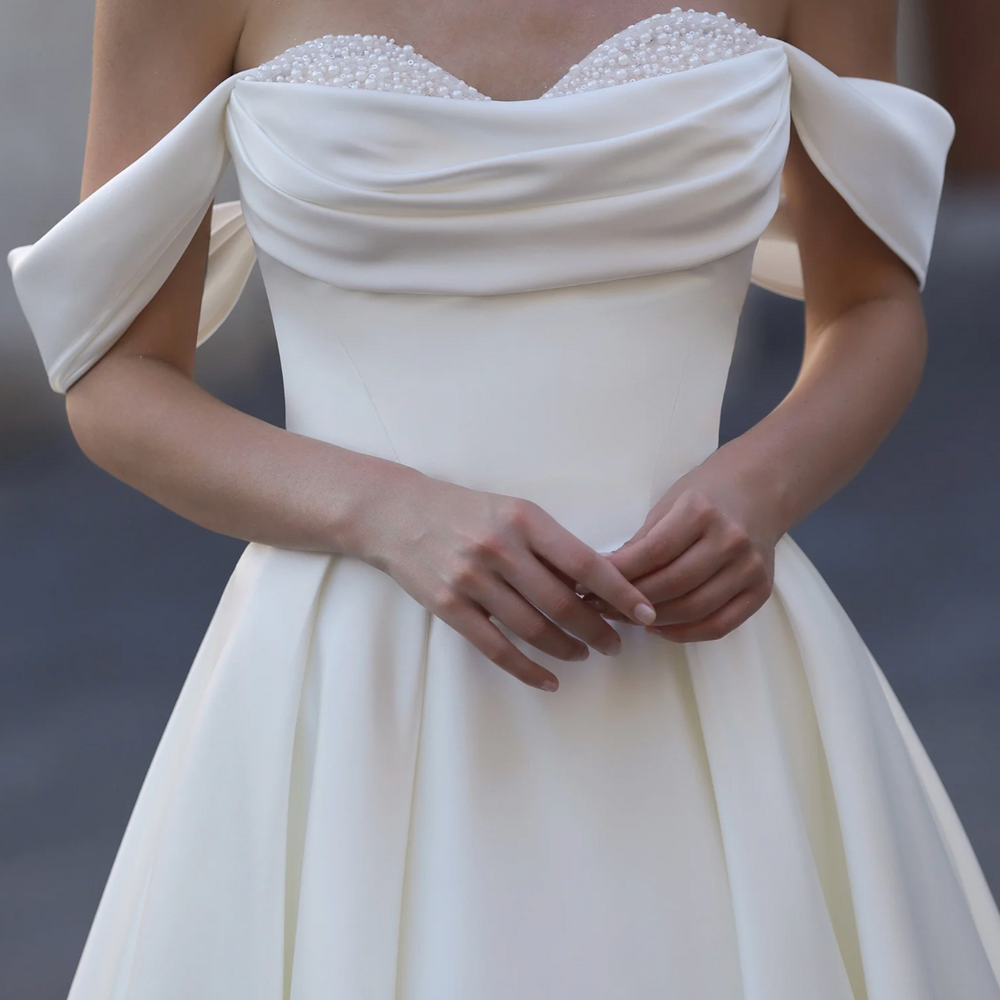 
                      
                        White off-shoulder dress with a bow detail, featuring the brand 'Ludyne Yuceed'.
                      
                    