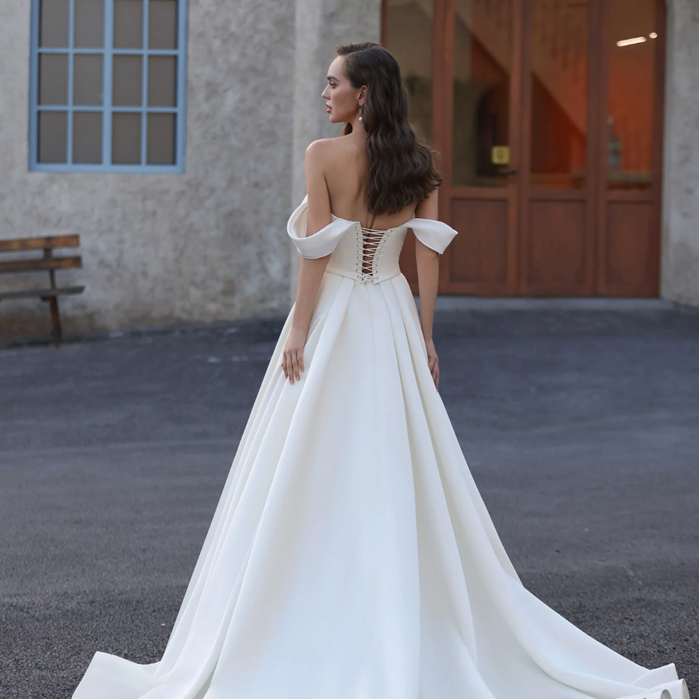 
                      
                        Woman in a white wedding dress with a flowing train standing in front of a building.
                      
                    