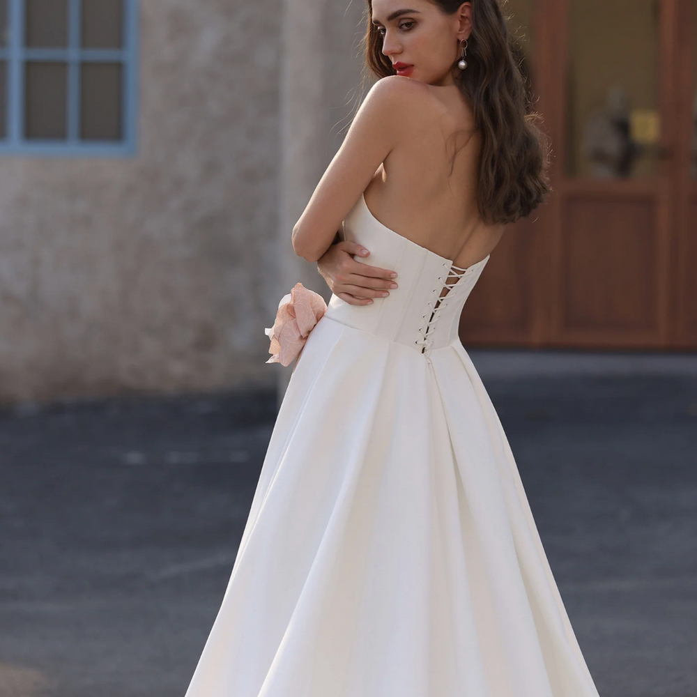 Woman in a white wedding dress with a backless design, standing in front of a building.