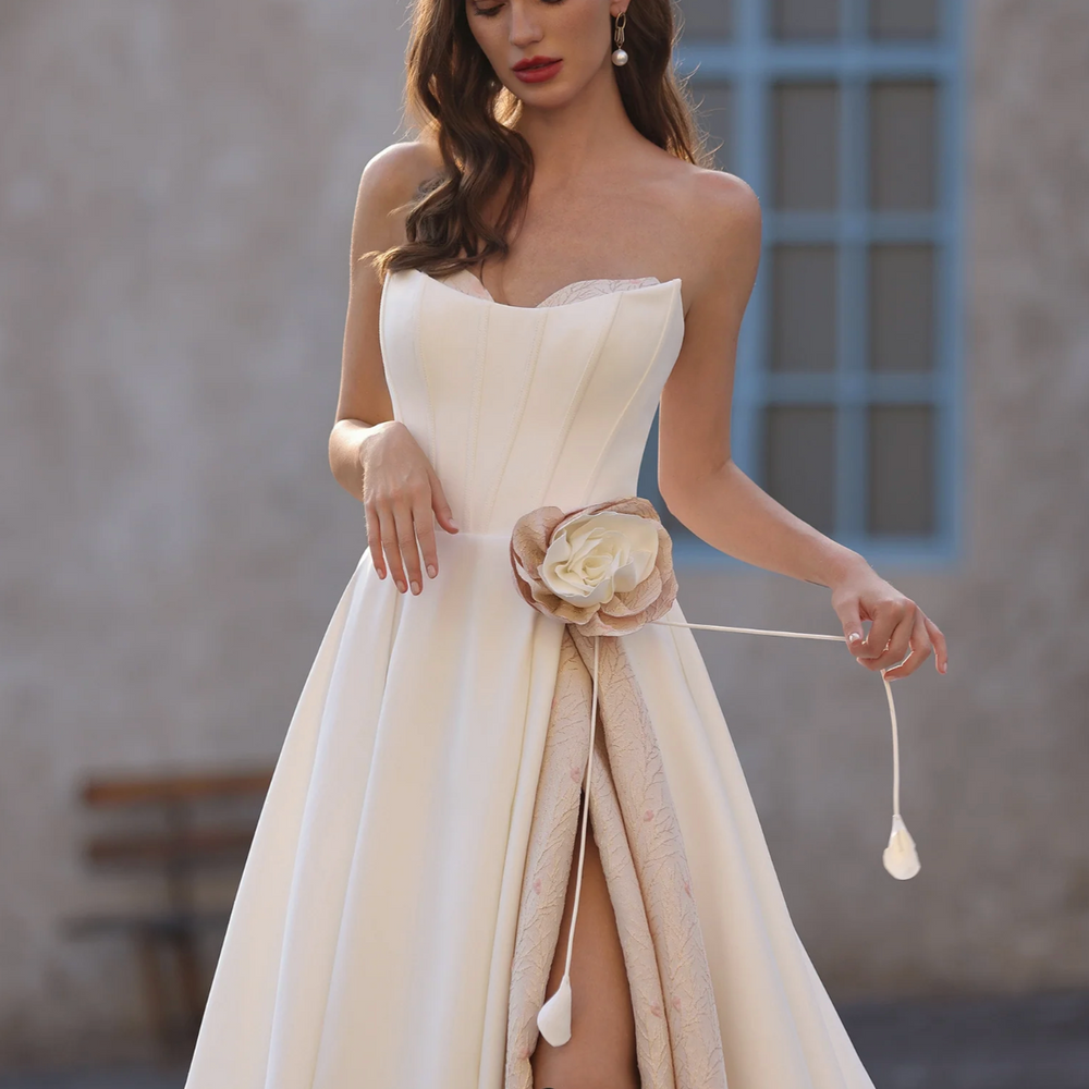 
                      
                        Woman in a strapless white dress with a floral sash standing against a neutral background
                      
                    