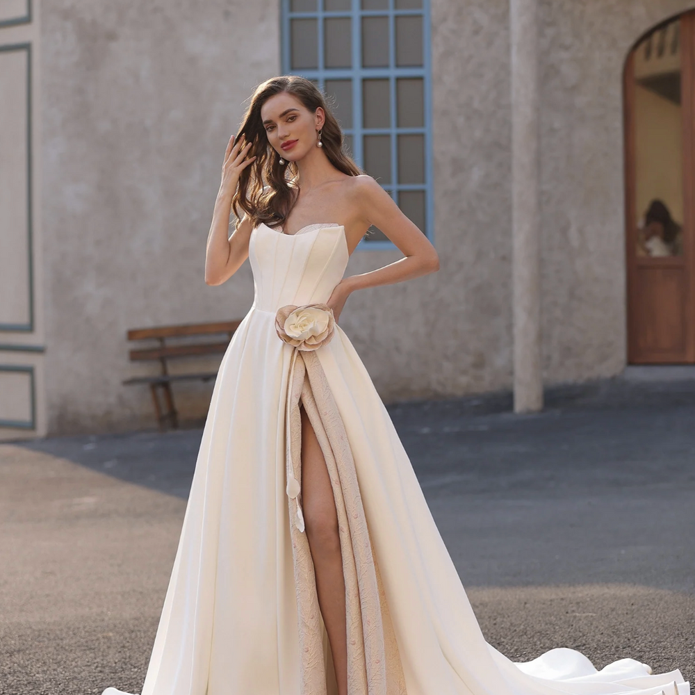 
                      
                        Woman in a white strapless gown with a high slit standing outdoors.
                      
                    