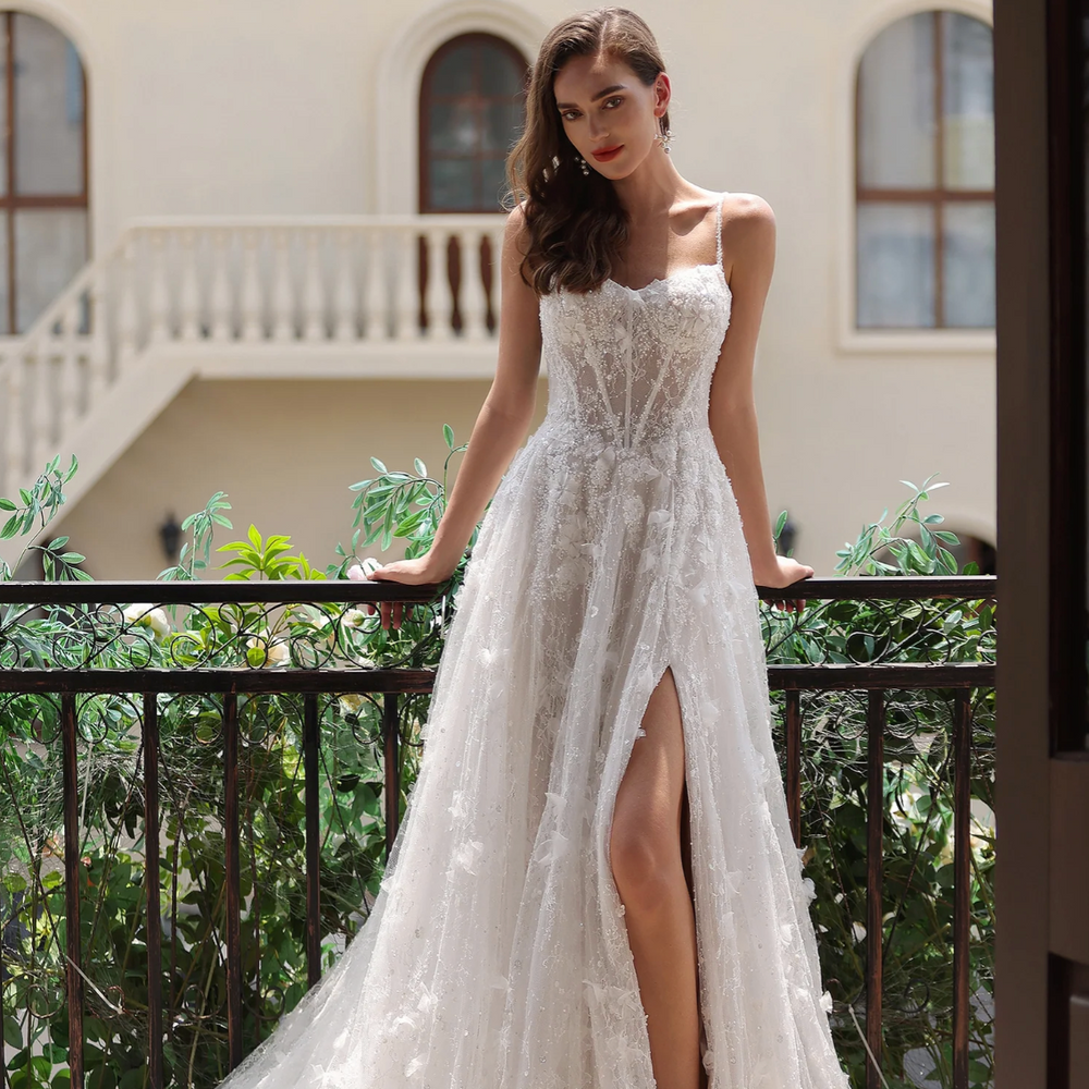 Romantic floral lace wedding gown with a high slit, spaghetti straps, and a flowing train, showcased outdoors.